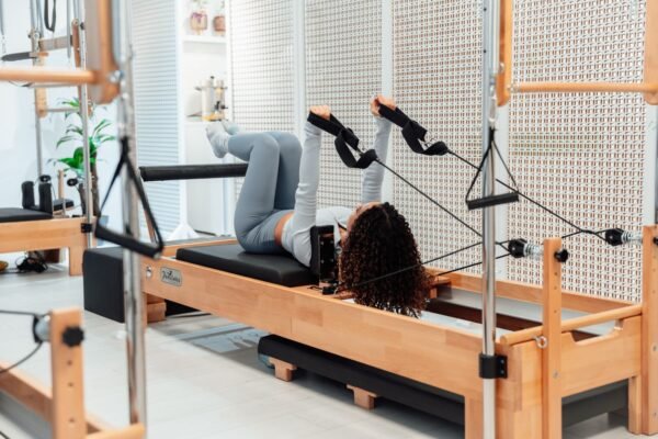 Pratiquante allongée sur un reformer en bois, les pieds dans les sangles