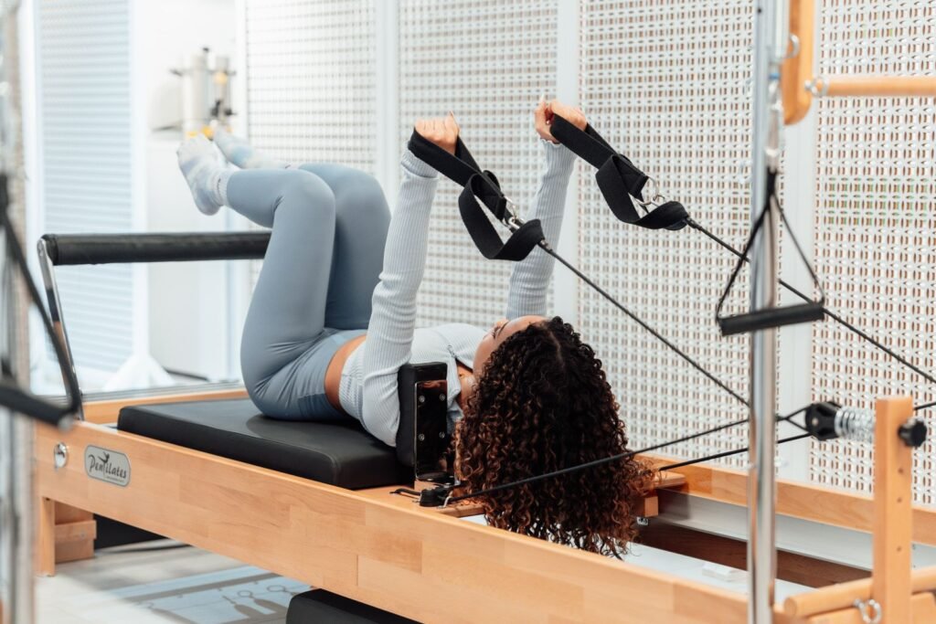 Femme allongée sur le chariot d'un reformer de studio, tirant sur les sangles reliées aux poulies