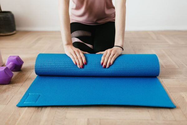 Femme à genoux déroulant un tapis de sport bleu sur un parquet, à la maison