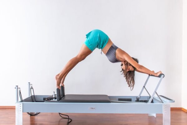 Femme en appui sur la barre d'un reformer Pilates à cadre métallique, dans une pièce au parquet clair